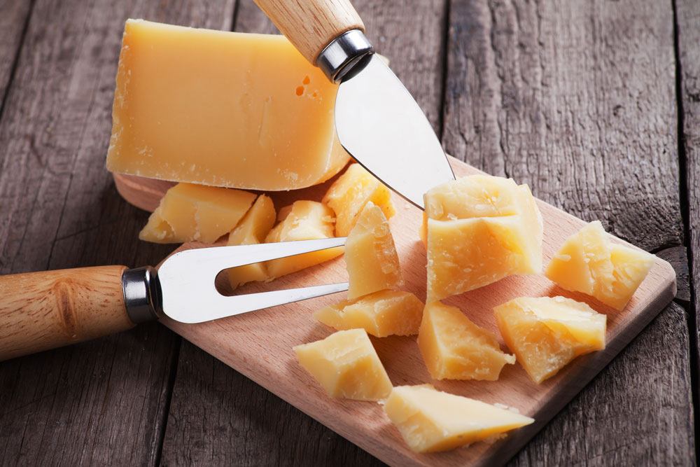 Sliced Grana Padano, a knife and a fork on the chopping board
