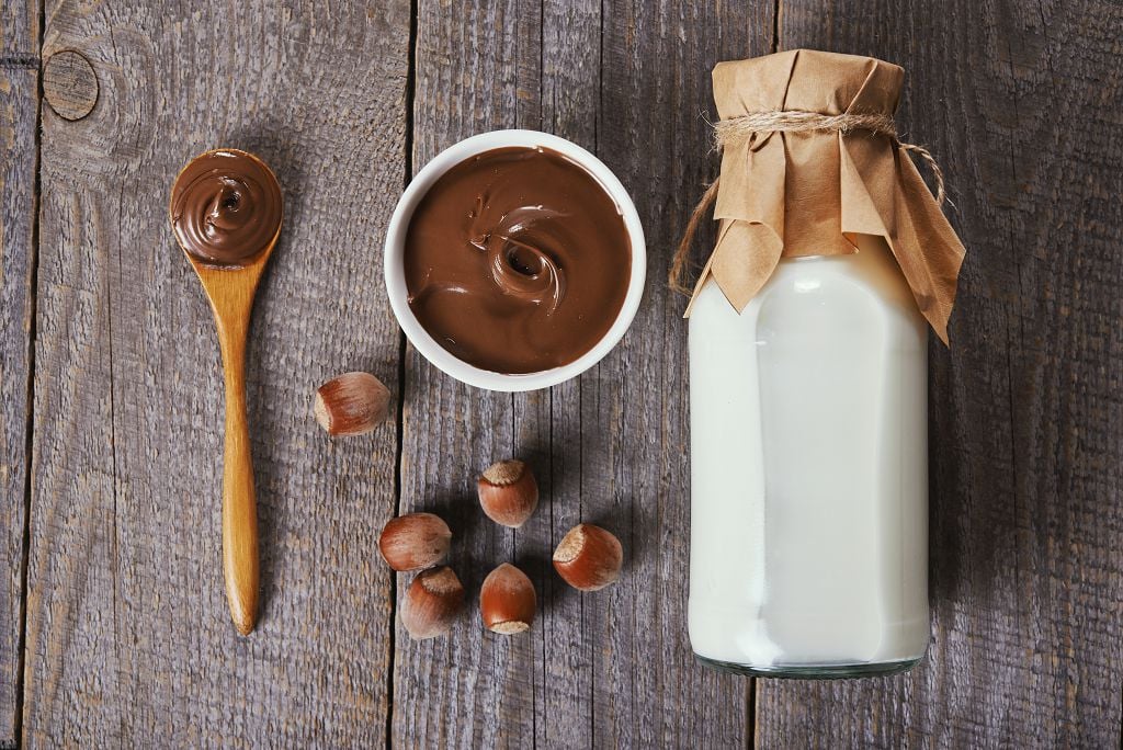 a spoon of melt natella, milk bottle and a bowl of melt nutella on the table