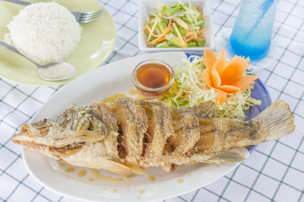 Lightly-Fried Snapper, fish sauce and vegetables on the plate, rice, a spoon and a fork