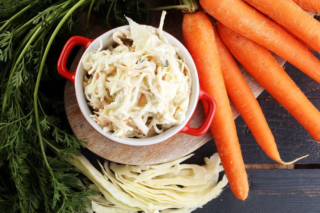 A pot of Coleslaw and carrots on the chopping board
