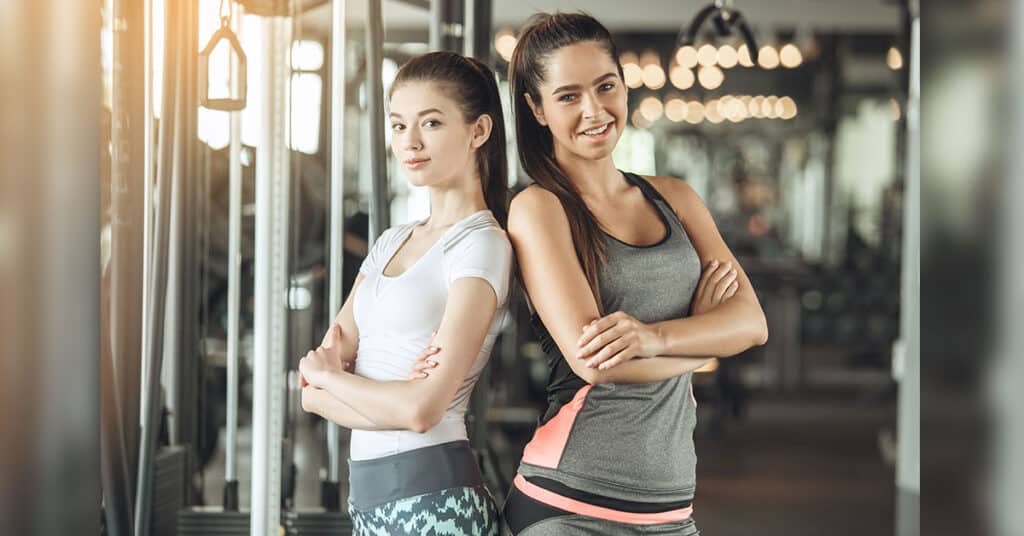 Two girls standing next to each other in workout clothing